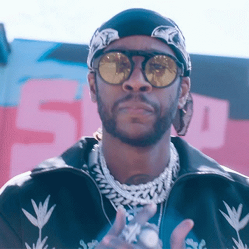 A Man Wearing Sunglasses And A Bandana Stands In Front Of A Sign That Says 5 GIF