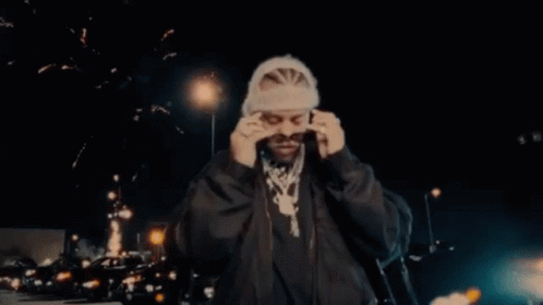 A Man Wearing Sunglasses And A Beanie Is Standing In Front Of Fireworks . GIF