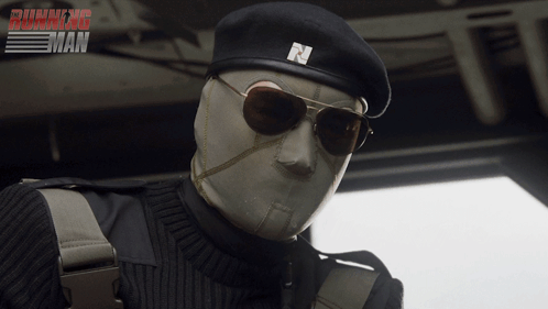 a man wearing sunglasses and a beret with the letter n on it is in front of a running man poster