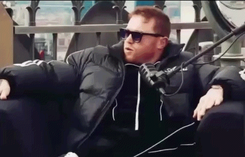 a man wearing sunglasses and a black jacket is sitting in a chair with a microphone .