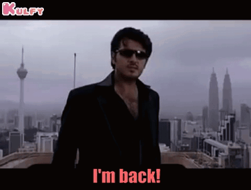A Man Wearing Sunglasses And A Black Jacket Is Standing In Front Of A City And Says I 'M Back . GIF