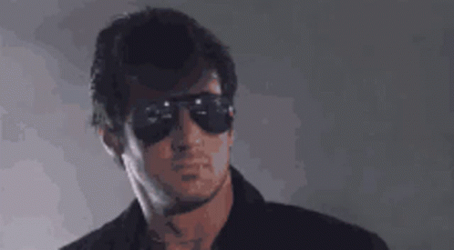 A Man Wearing Sunglasses And A Black Shirt Is Looking At The Camera . GIF