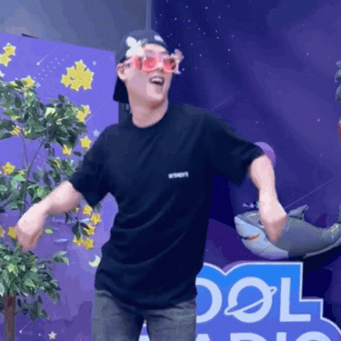 A Man Wearing Sunglasses And A Black Shirt Stands In Front Of A Sign That Says Cool GIF