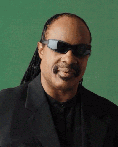 A Man Wearing Sunglasses And A Black Suit Is Smiling GIF