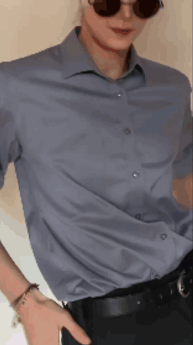 A Man Wearing Sunglasses And A Blue Shirt Holds His Hand In His Pocket GIF