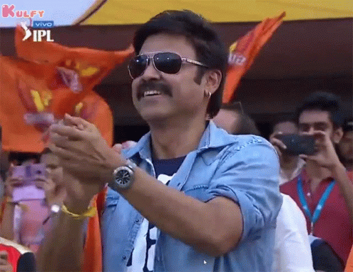 A Man Wearing Sunglasses And A Blue Shirt Is Clapping His Hands In Front Of A Crowd . GIF
