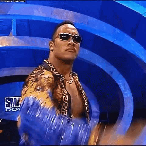 A Man Wearing Sunglasses And A Blue Shirt Is Standing In Front Of A Blue Background . GIF