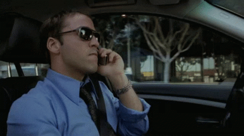 A Man Wearing Sunglasses And A Blue Shirt Is Talking On A Cell Phone GIF