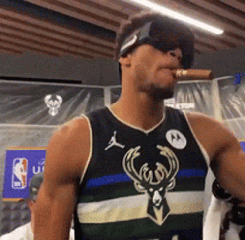 A Man Wearing Sunglasses And A Bucks Jersey Is Smoking A Cigar GIF