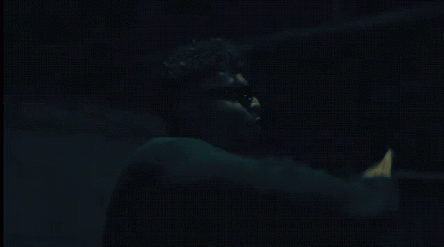 A Man Wearing Sunglasses And A Choker Is Standing In A Dark Room GIF