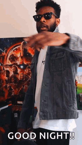 a man wearing sunglasses and a denim jacket is standing in front of a marvel poster and says good night .