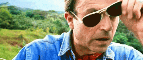 A Man Wearing Sunglasses And A Denim Shirt Is Looking At Something . GIF
