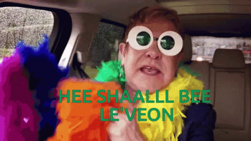 A Man Wearing Sunglasses And A Feather Boa Says " Hee Shaall Bee Le Veon " GIF