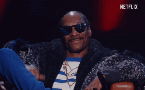 A Man Wearing Sunglasses And A Fur Coat Is Sitting In Front Of A Netflix Sign GIF