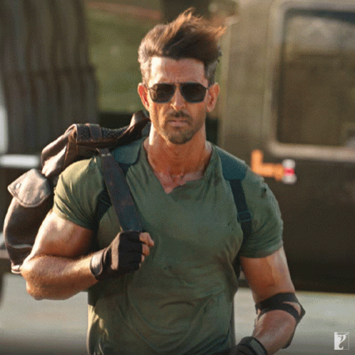 A Man Wearing Sunglasses And A Green Shirt Carrying A Brown Bag GIF