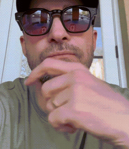A Man Wearing Sunglasses And A Hat Holds His Hand To His Mouth GIF