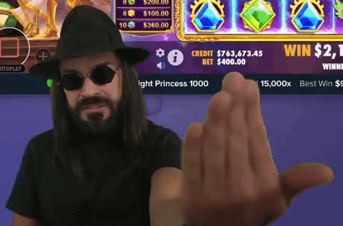 A Man Wearing Sunglasses And A Hat Holds Up His Hand In Front Of A Screen That Says Win $ 2.1 GIF