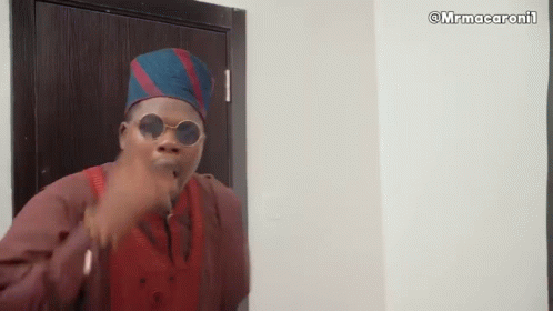 A Man Wearing Sunglasses And A Hat Is Standing In Front Of A Door And Making A Funny Face . GIF