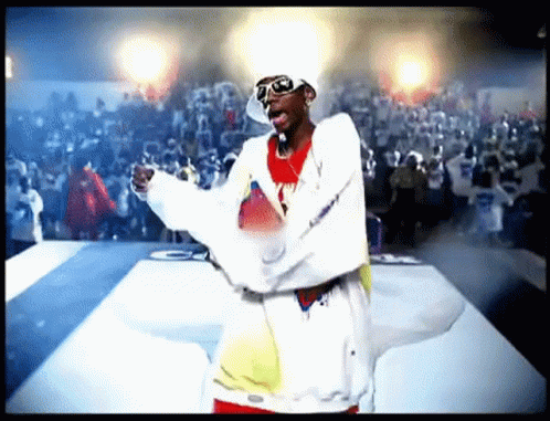 A Man Wearing Sunglasses And A Hat Is Standing On A Stage With His Arms Outstretched In Front Of A Crowd . GIF