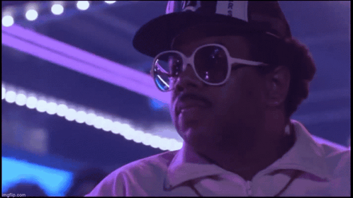 A Man Wearing Sunglasses And A Hat With The Letter A On It Looks At The Camera GIF