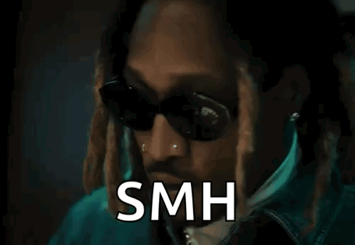 a man wearing sunglasses and a jacket is standing in front of a door with the word smh written on it .
