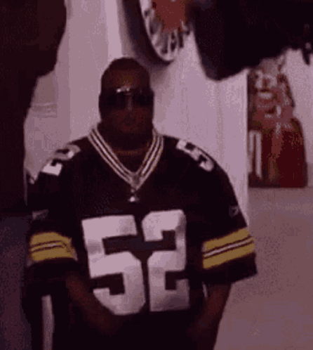 A Man Wearing Sunglasses And A Jersey With The Number 52 On It Is Standing In A Room . GIF