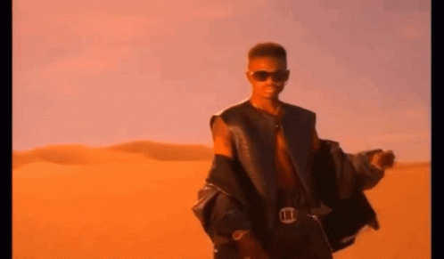 A Man Wearing Sunglasses And A Leather Jacket Is Standing In The Desert . GIF