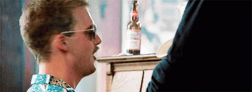 A Man Wearing Sunglasses And A Mustache Is Sitting At A Table With A Bottle Of Beer . GIF