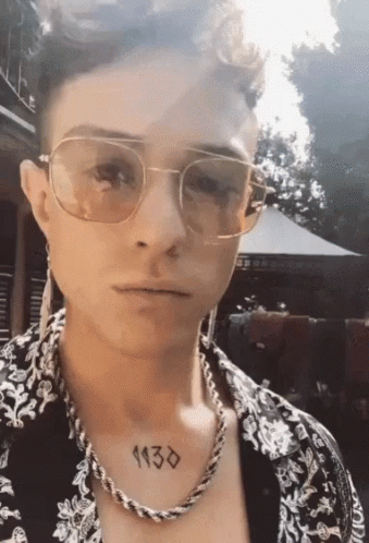A Man Wearing Sunglasses And A Necklace Has A Tattoo On His Chest That Reads 1130 GIF