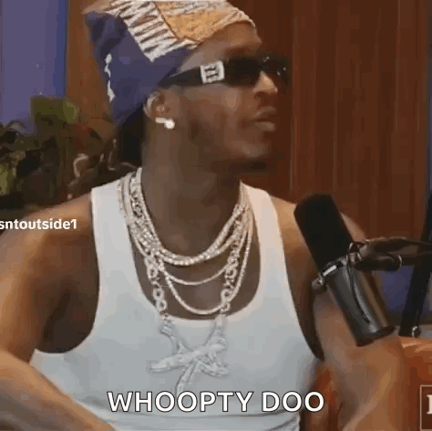 A Man Wearing Sunglasses And A Necklace Is Sitting In Front Of A Microphone And Says Whoopty Doo . GIF