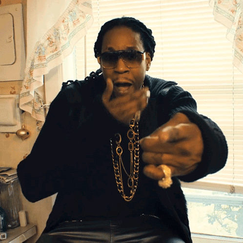 A Man Wearing Sunglasses And A Necklace Is Sitting In Front Of A Window In A Kitchen GIF