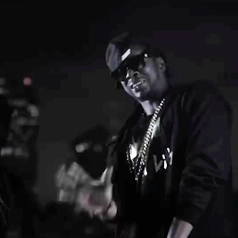 A Man Wearing Sunglasses And A Necklace Is Standing In The Dark . GIF