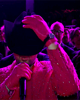 A Man Wearing Sunglasses And A Pink Jacket Is Holding A Microphone GIF
