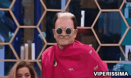 A Man Wearing Sunglasses And A Pink Shirt Is Standing In Front Of A Honeycomb Shelf . GIF