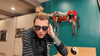 A Man Wearing Sunglasses And A Ponytail Stands In Front Of A Zebra Statue GIF