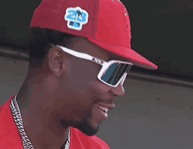 A Man Wearing Sunglasses And A Red Hat Smiles GIF