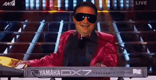 A Man Wearing Sunglasses And A Red Jacket Is Playing A Yamaha Dx7 Keyboard GIF