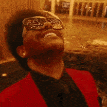 A Man Wearing Sunglasses And A Red Jacket Looks Up At The Sky GIF