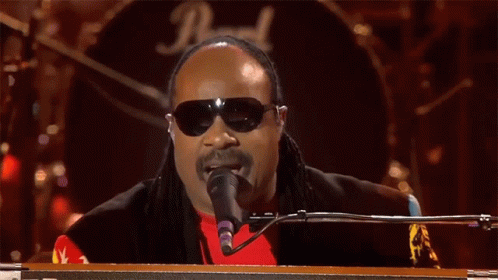 A Man Wearing Sunglasses And A Red Shirt Is Singing Into A Microphone In Front Of A Drum Set With The Letter D On It GIF