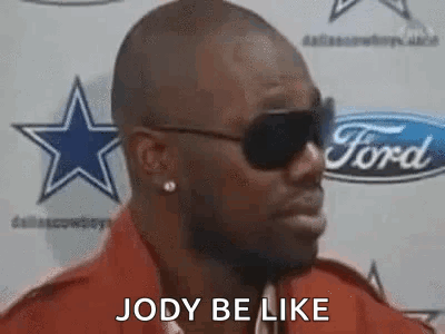 A Man Wearing Sunglasses And A Red Shirt Is Standing In Front Of A Ford Sign . GIF