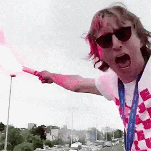 A Man Wearing Sunglasses And A Scarf Is Holding A Flare In His Hand . GIF