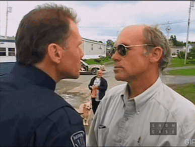A Man Wearing Sunglasses And A Show Case Shirt Talks To A Police Officer GIF