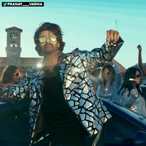 A Man Wearing Sunglasses And A Silver Jacket Is Dancing GIF