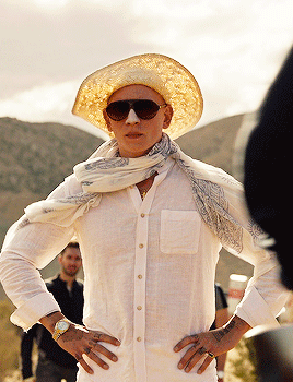 a man wearing sunglasses and a straw hat stands with his hands on his hips