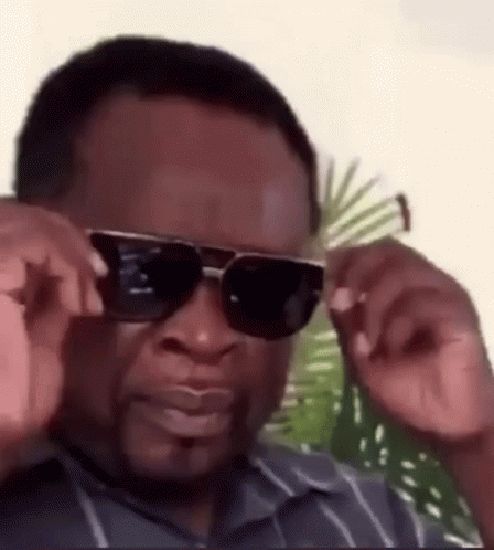 A Man Wearing Sunglasses And A Striped Shirt Is Adjusting His Sunglasses . GIF