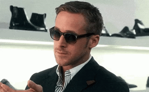 A Man Wearing Sunglasses And A Suit Is Standing In Front Of A Shelf With Shoes . GIF