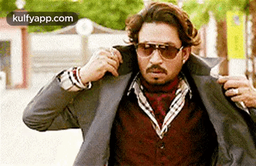 A Man Wearing Sunglasses And A Suit Jacket Is Being Helped By Another Man . GIF