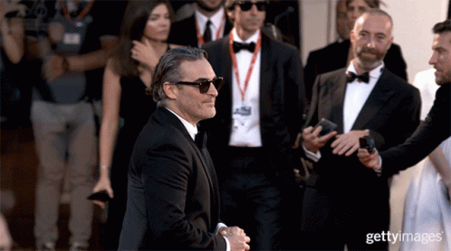 A Man Wearing Sunglasses And A Tuxedo Is Being Escorted By A Group Of Men GIF