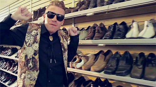 a man wearing sunglasses and a vest with a dog on it stands in front of a wall of shoes