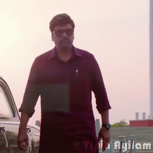 A Man Wearing Sunglasses And A Watch Is Standing In Front Of A Car With The Word Ayilam On The Bottom Right GIF